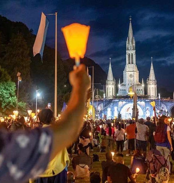 Lourdes candles at night arm pilgrimage tour